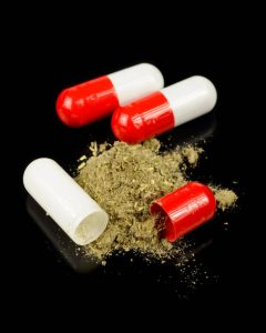 Opened and unopened capsules with dried herb on black background