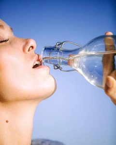 A woman drinking water from a glass bottle